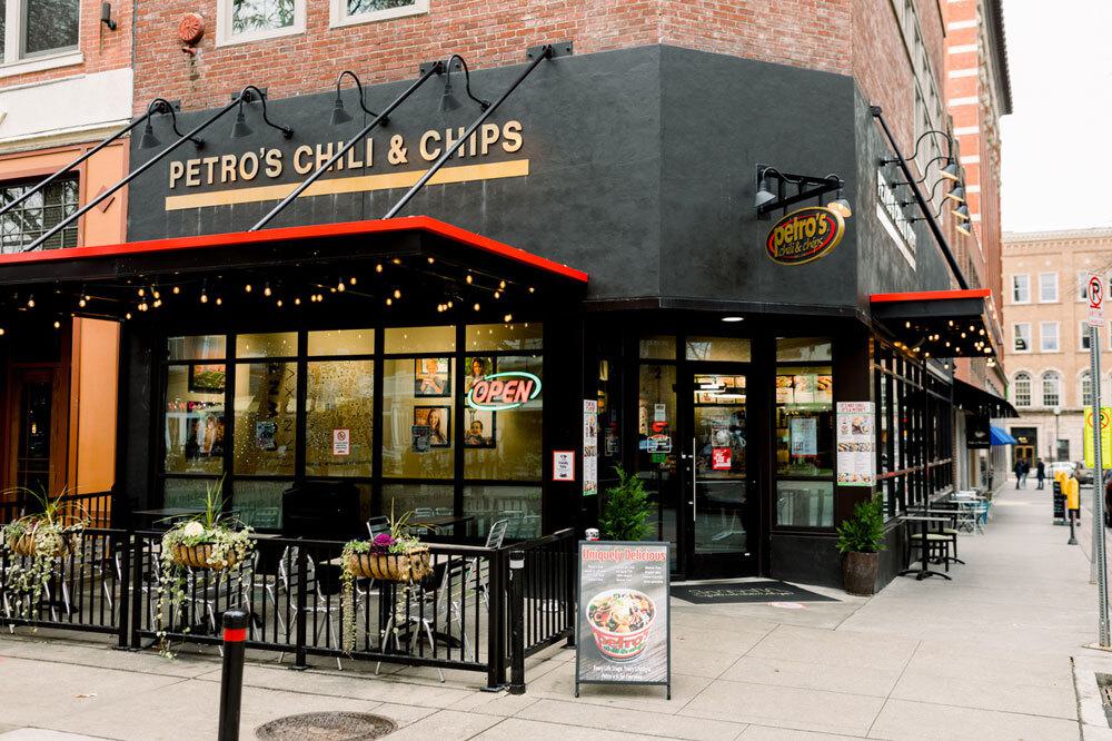 Corner restaurant storefront with black awning, red trim, and gold lettering reading 'PETRO'S CHILI & CHIPS'