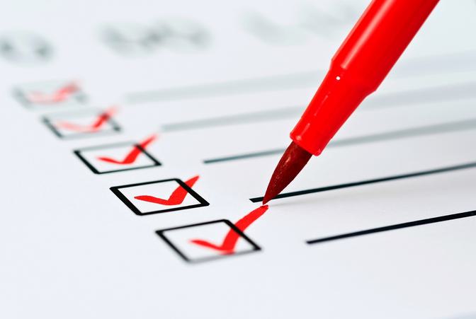 Red marker pen checking off boxes on a printed checklist, close-up product/business photo with red checkmarks on white paper