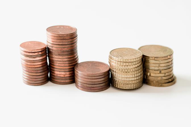 Five stacks of British coins arranged on white background—pennies, pence, and pounds—studio product photography