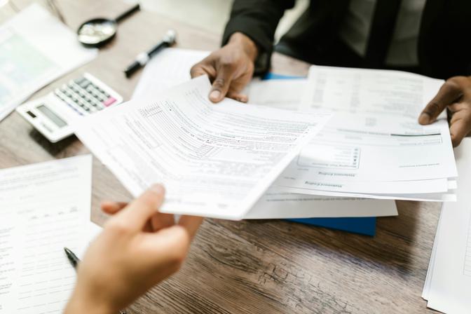 Two people reviewing financial documents and spreadsheets at a wooden desk with calculator