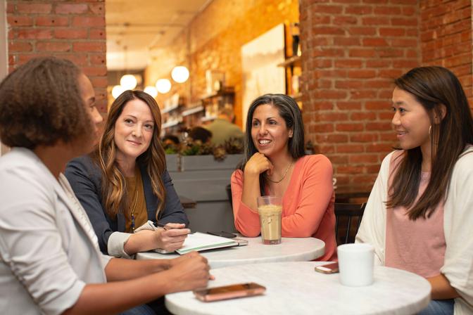 Four diverse women in casual business attire seated around a white table in a modern brick-walled office