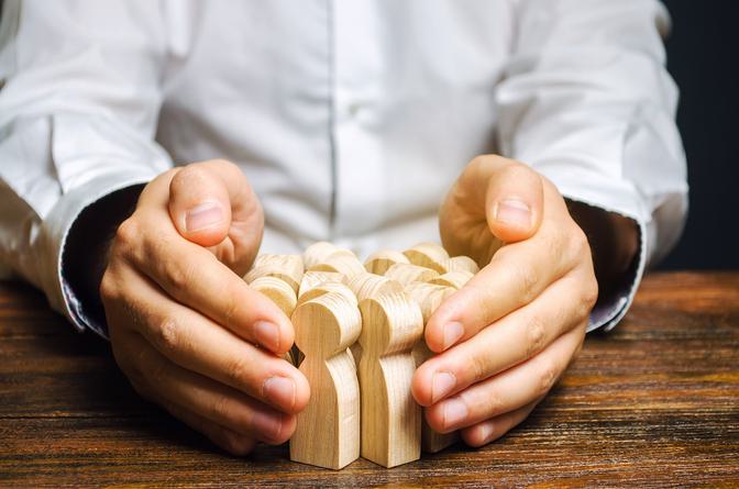 Hands sheltering wooden blocks arranged in a line on a wooden table, white shirt and dark sleeves